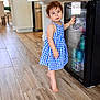 Raea joined the competition — help win amazing prizes! toddler, child, blue_dress, barefoot, kitchen, wooden_floor, mini_fridge, cans, snacks, plastic_cups, glass_door, curious, standing, indoor, home, appliance, food, drink, person, flooring