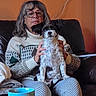 black_and_white_dog, blanket, cable_on_wall, couch, cozy, dog, glasses, hands, indoor, lap, living_room, mug, patterned_pants, person, pet, portrait, seated, smartphone, sofa, sweater