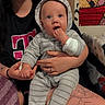 baby, infant, child, adult, parent, portrait, indoors, sitting, onesie, hood, bunny_ears, gray_clothing, blue_eyes, hand_in_mouth, smiling, family, holding_baby, colorful_artwork, couch, tattoo