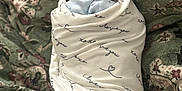 Roman is registered to the contest to win money with this photo: newborn, baby, sleeping, blanket, swaddle, face, infant, resting, soft_lighting, portrait, closeup, fabric, pattern, floral, green, white, text_on_blanket, peaceful, cute, indoors