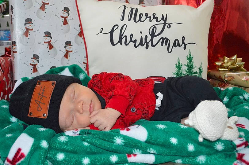 Axton is registered to the contest to win money with this photo: child, christmas, christmas_decoration, christmas_eve, comfort, event, font, green, handwriting, hat, headwear, holiday, lap, linens, pattern, people, person, red, room, textile