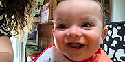 Louison participe au concours pour gagner de l'argent avec cette photo : baby, smiling, indoor, bib, orange_clothing, curly_hair, wooden_furniture, smile, happy, face, person, child, messy_face, cabinet, basket, radio, chair, home, closeup, portrait