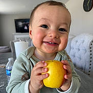 Yusuf joined the competition — help win amazing prizes! baby, child, smile, apple, hands, face, indoor, clothing, table, water_bottle, television, clock, chair, furniture, happy, cute, skin, eyelashes, home, person