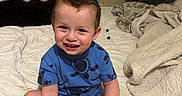 Hector is registered to the contest to win money with this photo: baby, bare_feet, bed, bed linens, bedroom, blanket, blue_clothing, boy, brown_hair, candid, child, face, happy, home, indoors, pajamas, portrait, sitting, smiling, toddler