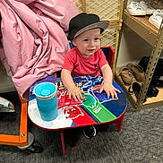 Hector joined the competition — help win amazing prizes! baby, child, infant, smiling, sitting, cap, hat, red_shirt, table, colorful, superhero, toy, cup, indoor, store, shelving, shoes, fabric, portrait, happy