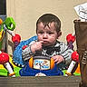 child, toddler, boy, sitting, toy_vehicle, ride_on_toy, playroom, indoor, portrait, face, serious, brown_hair, jacket, clothing, hands, steering_wheel, colorful, furniture, home, photograph