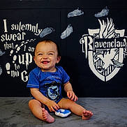 Ezra joined the competition — help win amazing prizes! baby, child, smiling, blue_clothing, onesie, sitting, footprints, harry_potter, ravenclaw, crest, wall_art, indoor, happy, cute, infant, portrait, playful, person, floor, background