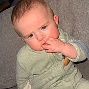 Gabriel participe au concours pour gagner de l'argent avec cette photo : baby, child, infant, face, fingers, couch, blanket, green_clothing, sitting, indoors, curious_expression, soft_texture, head, person, young, cozy, home, cute, comfort, portrait
