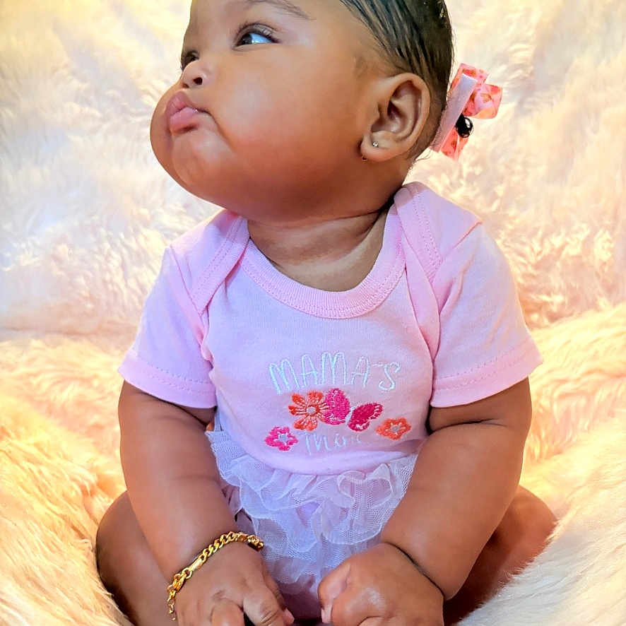 Veda is registered to the contest to win money with this photo: baby, infant, pink_clothing, bracelet, bow, pout, fluffy_blanket, sitting, cute, indoors, portrait, child, soft_texture, adorable, young_child, skin, hand, foot, curious, toddler