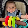 baby, stroller, smiling, child, plush_toy, toy, blue_clothing, head, face, seat, sitting, hand, foot, fabric, comfort, infant, casual_clothing, happy, indoor, baby_bib