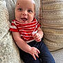 baby, smiling, couch, red_striped_bib, navy_pants, infant, happy, sitting, indoor, face, skin, child, clothing, cute, portrait, cozy, cushion, home, person, young_child