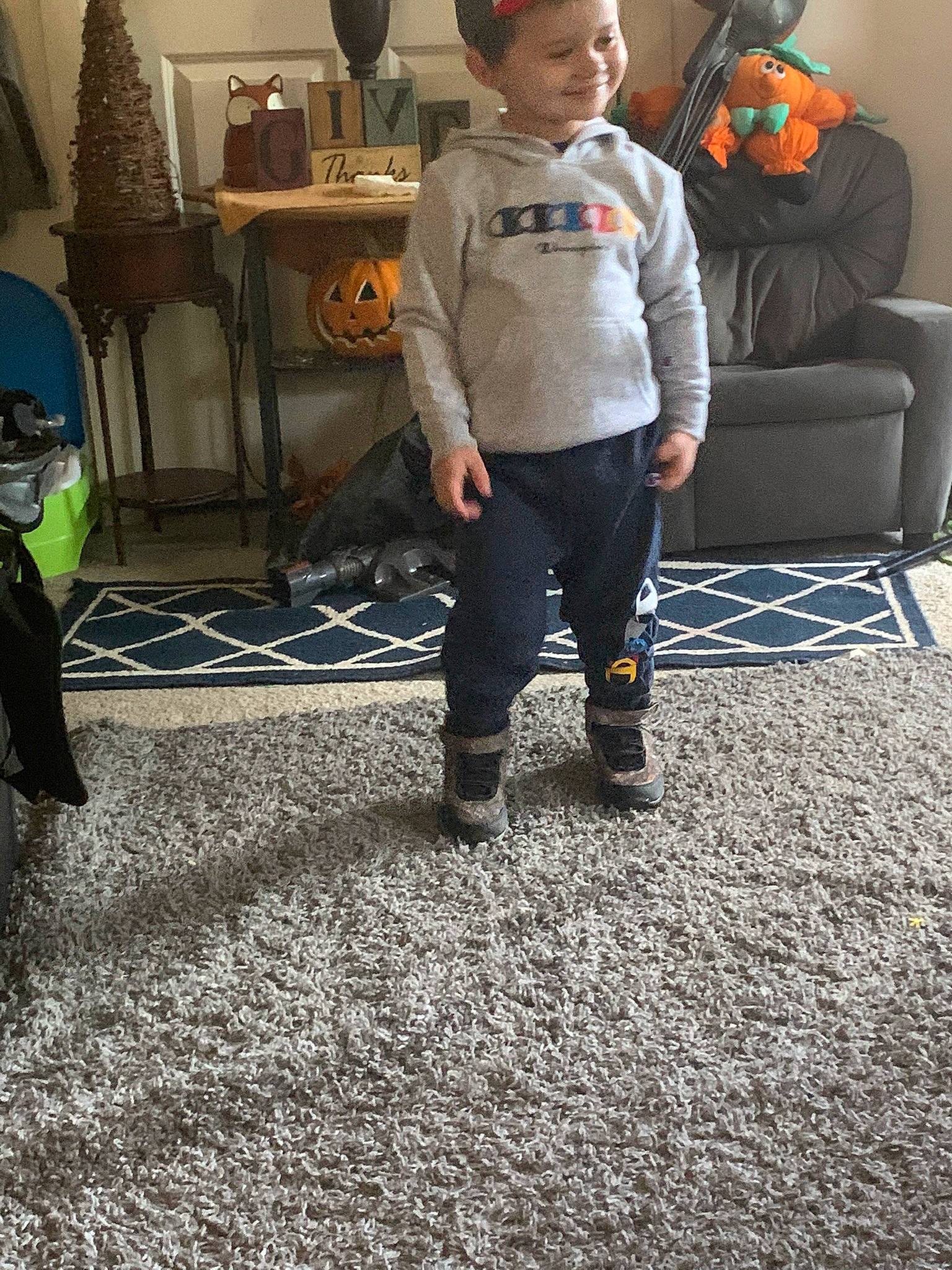 Brantley is registered to the contest to win money with this photo: boot, carpet, child, comfort, couch, event, floor, flooring, fun, hardwood, houseplant, human_leg, joy, living_room, person, room, sitting, smile, sneakers, standing