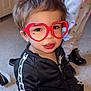 toddler, child, glasses, red_glasses, heart_shaped_glasses, black_tracksuit, nike, pajamas, carpet, indoor, person, footwear, playing, cute, smiling, hair, face, fashion, childhood, home