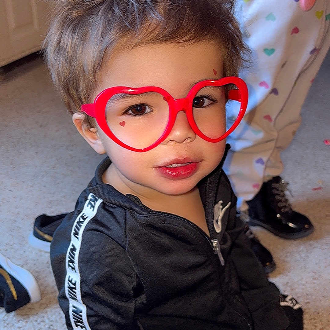 Miliano is registered to the contest to win money with this photo: black_tracksuit, carpet, child, childhood, cute, face, fashion, footwear, glasses, hair, heart_shaped_glasses, home, indoor, nike, pajamas, person, playing, red_glasses, smiling, toddler