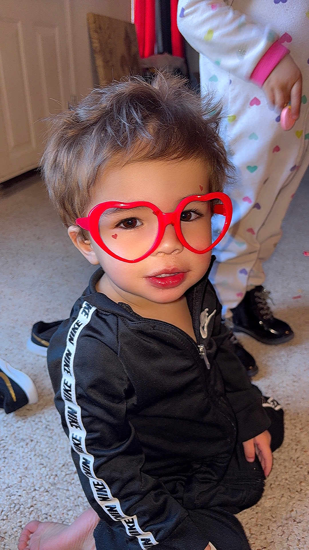 Miliano is registered to the contest to win money with this photo: toddler, child, glasses, red_glasses, heart_shaped_glasses, black_tracksuit, nike, pajamas, carpet, indoor, person, footwear, playing, cute, smiling, hair, face, fashion, childhood, home