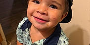 Miliano is registered to the contest to win money with this photo: toddler, child, smiling, face, cap, shirt, indoor, floor, wooden_floor, person, happy, drawing_on_face, clothing, short_sleeves, looking_up, barefoot, hands, wall, home, casual