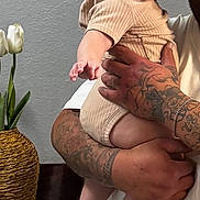 Ainsley joined the competition — help win amazing prizes! baby, child, person, tattoo, hand, face, headband, socks, plant, flower, vase, indoor, table, wall, adult, holding, cute, smile, cozy, portrait