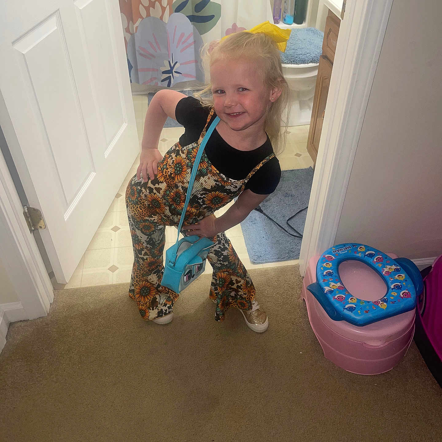 Gracelynne joined the competition — help win amazing prizes! accessory, bathroom, blue_purse, cabinet, carpet, child, cute, door, fashion, floor, floral_jumpsuit, girl, happy, home_interior, posing, potty_chair, shower_curtain, smiling, toiletries, yellow_bow