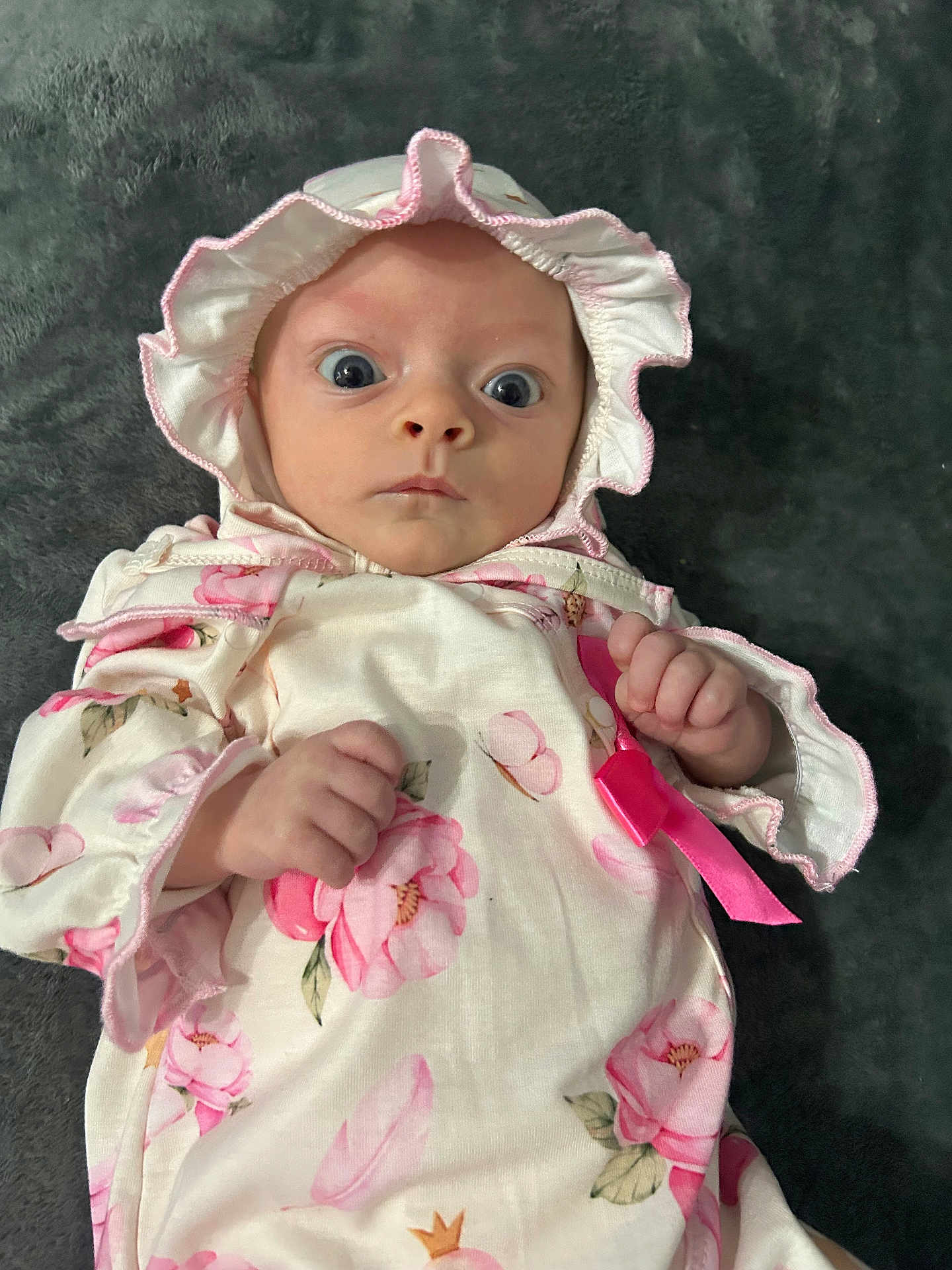 Arabella joined the competition — help win amazing prizes! baby, infant, child, face, wide_eyes, bonnet, clothing, floral, pink, onesie, hand, lying_down, blanket, portrait, cute, expression, soft_texture, indoors, newborn, adorable