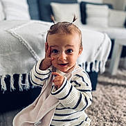 Mila a rejoint le concours — aidez-le/la à gagner de superbes lots ! toddler, child, baby, striped_clothing, knitwear, pigtails, blanket, carpet, living_room, couch, throw_blanket, curious_expression, sitting, indoor, soft_lighting, person, cute, playful, home, portrait