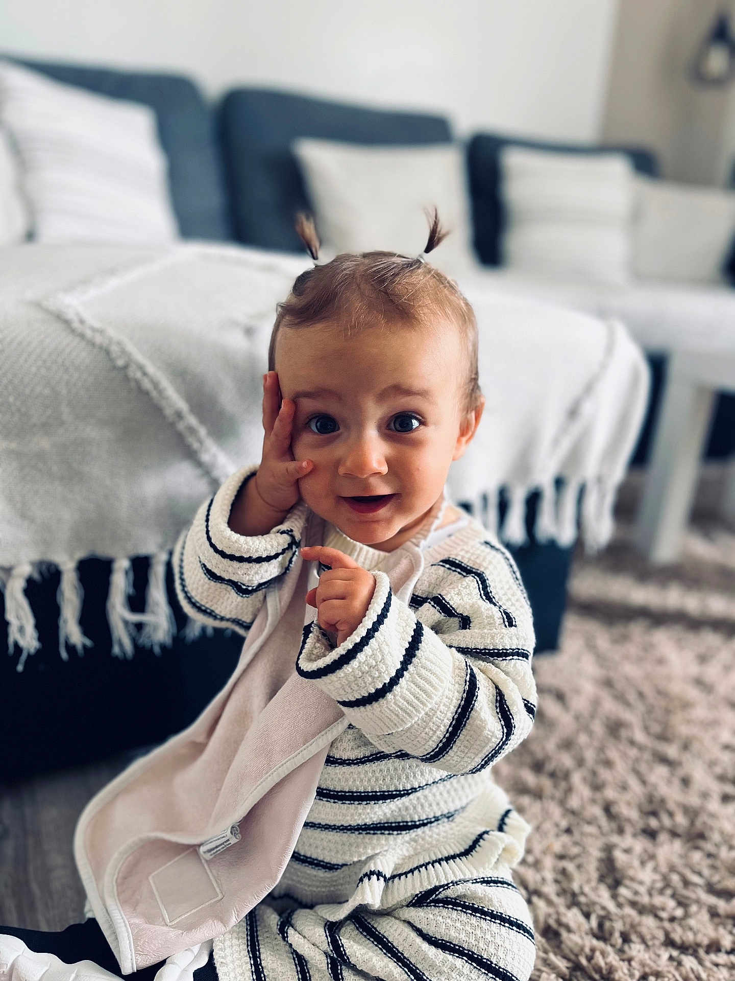 Mila a rejoint le concours — aidez-le/la à gagner de superbes lots ! toddler, child, baby, striped_clothing, knitwear, pigtails, blanket, carpet, living_room, couch, throw_blanket, curious_expression, sitting, indoor, soft_lighting, person, cute, playful, home, portrait