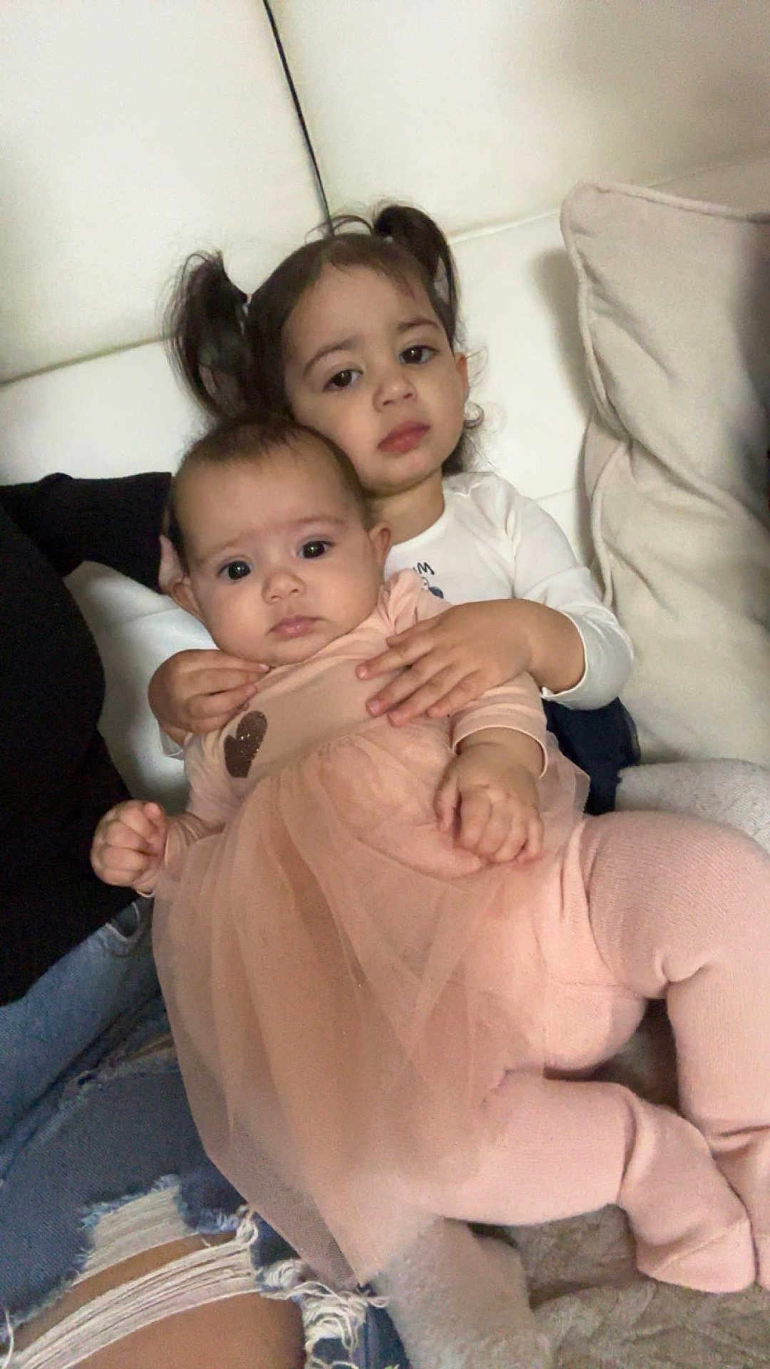 Layanah a rejoint le concours — aidez-le/la à gagner de superbes lots ! baby, child, sibling, tutu, pink_clothing, white_clothing, couch, cushion, indoor, portrait, holding, cute, family, toddler, seated, face, person, young, home, cozy