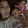 woman, baby, child, tongue_out, selfie, family, cute, indoor, pink_clothing, white_lace, patterned_pillow, face, head, skin, expression, holding, portrait, sitting, relaxed, playful