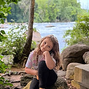 Brooklinn joined the competition — help win amazing prizes! casual_clothing, child, curly_hair, daylight, footwear, forest, girl, greenery, happy, leaves, nature, outdoor, portrait, relaxing, river, rock, scenic, sitting, smile, tree