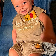Stephen is registered to the contest to win money with this photo: baby, child, smiling, blue_eyes, winnie_the_pooh, clothing, shorts, tshirt, blanket, indoor, person, happy, cute, infant, reaching_hand, portrait, sitting, soft_texture, fabric, playful