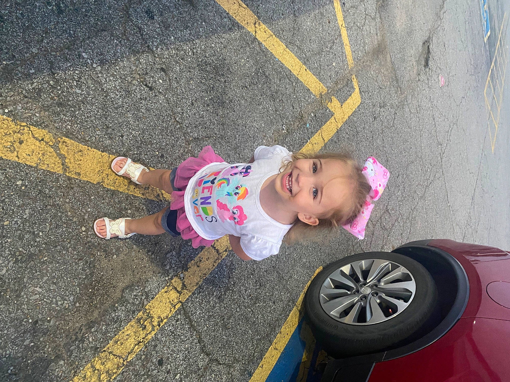Lyra is registered to the contest to win money with this photo: alloy_wheel, asphalt, automotive_exterior, automotive_tire, bumper, car, child, fender, fun, grass, joy, person, plant, rim, road_surface, sidewalk, sneakers, synthetic_rubber, tire, toddler