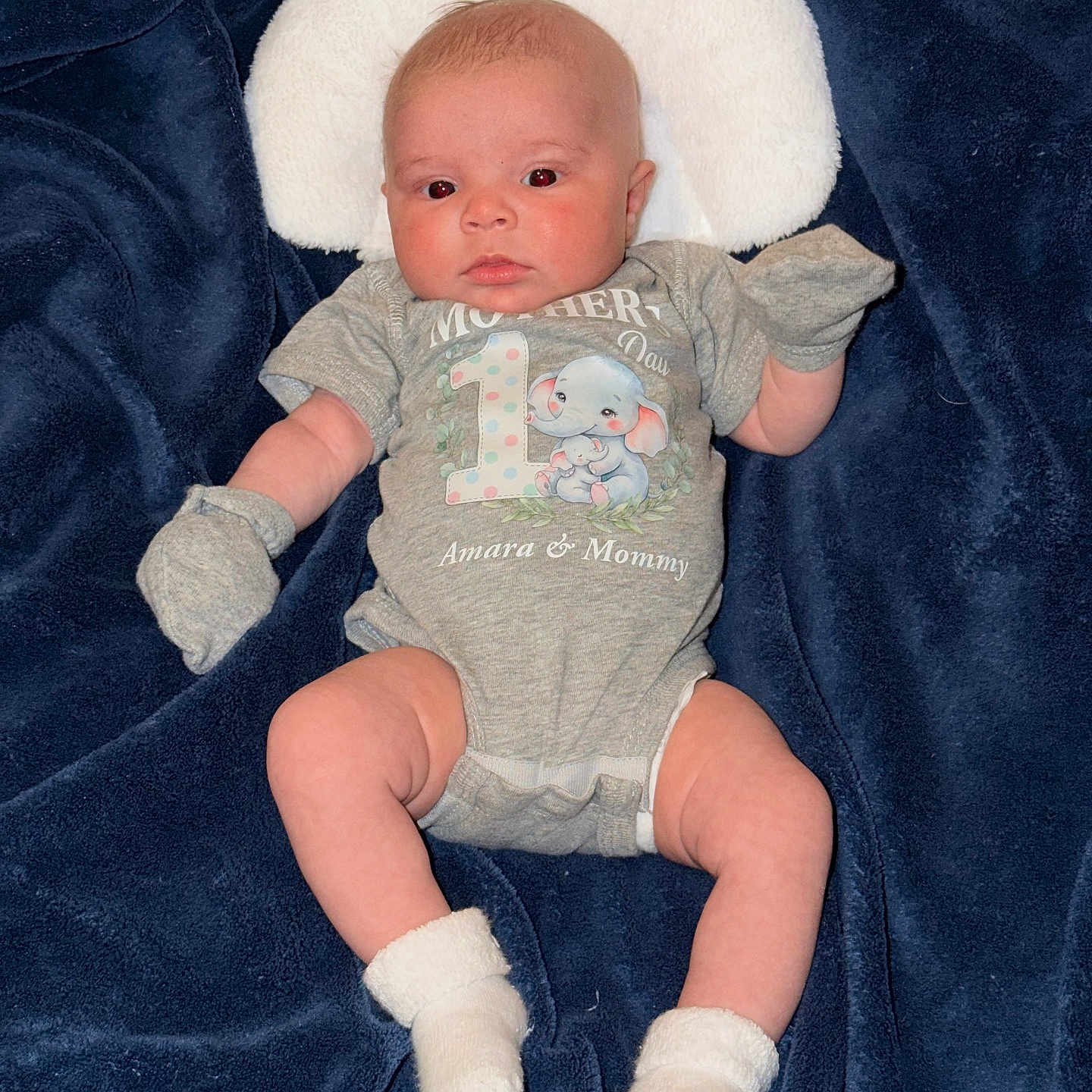 Amara is registered to the contest to win money with this photo: baby, infant, onesie, mittens, socks, blanket, pillow, cute, newborn, face, lying_down, clothing, soft, blue, grey, elephant, text, person, portrait, indoors