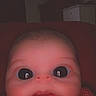 baby, face_filter, distorted_face, big_eyes, infant, closeup, indoors, dim_light, funny, portrait, child, red_clothing, cute, head, expression, skin, baby_face, digital_effect, young_child, background_furniture