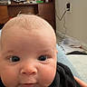 baby, infant, face, eyes, black_shirt, chubby_cheeks, indoor, living_room, shelf, television, couch, person, cute, young_child, portrait, casual, home, expression, child, closeup