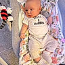 Amara is registered to the contest to win money with this photo: baby, infant, baby_rocker, blanket, soft_toy, clothing, socks, carpet, floor, indoor, person, cute, cozy, child, portrait, smiling, toddler, toy, pacifier, fabric