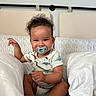 Wave is registered to the contest to win money with this photo: baby, bed, child, cozy, curly_hair, cute, dinosaur_print, happy, indoor, infant, onesie, pacifier, person, pillow, portrait, sitting, skin, smile, white_bedding, young_child
