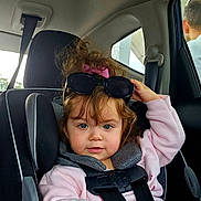 Victoria is registered to the contest to win money with this photo: child, toddler, car_seat, seatbelt, sunglasses, pink_sweater, hair_bow, curly_hair, blue_eyes, buckle, hand, car_interior, window, backseat, portrait, candid, baby, headrest, clothing, passenger