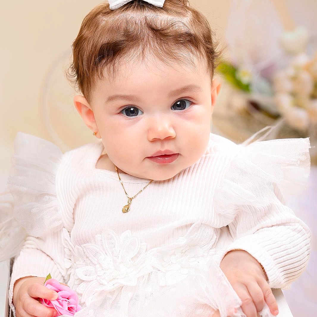 Kalyna is registered to the contest to win money with this photo: adorable, baby, bow, child, close_up, curious, cute, earrings, flower, indoor, infant, jewelry, lace, necklace, pink_flower, portrait, sitting, soft_lighting, tulle, white_dress