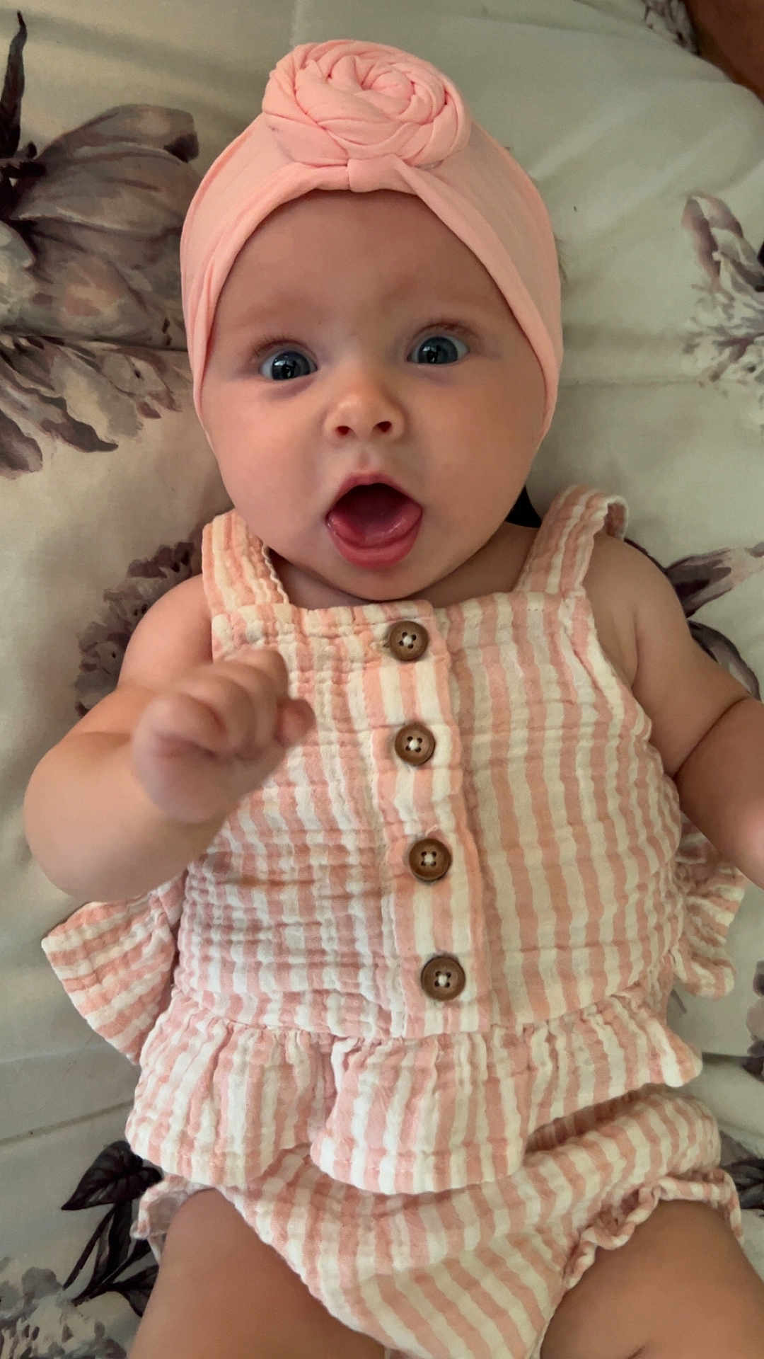 Amelia is registered to the contest to win money with this photo: baby, infant, child, pink_headband, striped_outfit, turban, buttons, floral_blanket, wide_eyes, open_mouth, cute, lying_down, clothing, adorable, expression, portrait, skin, hand, fingers, young_child