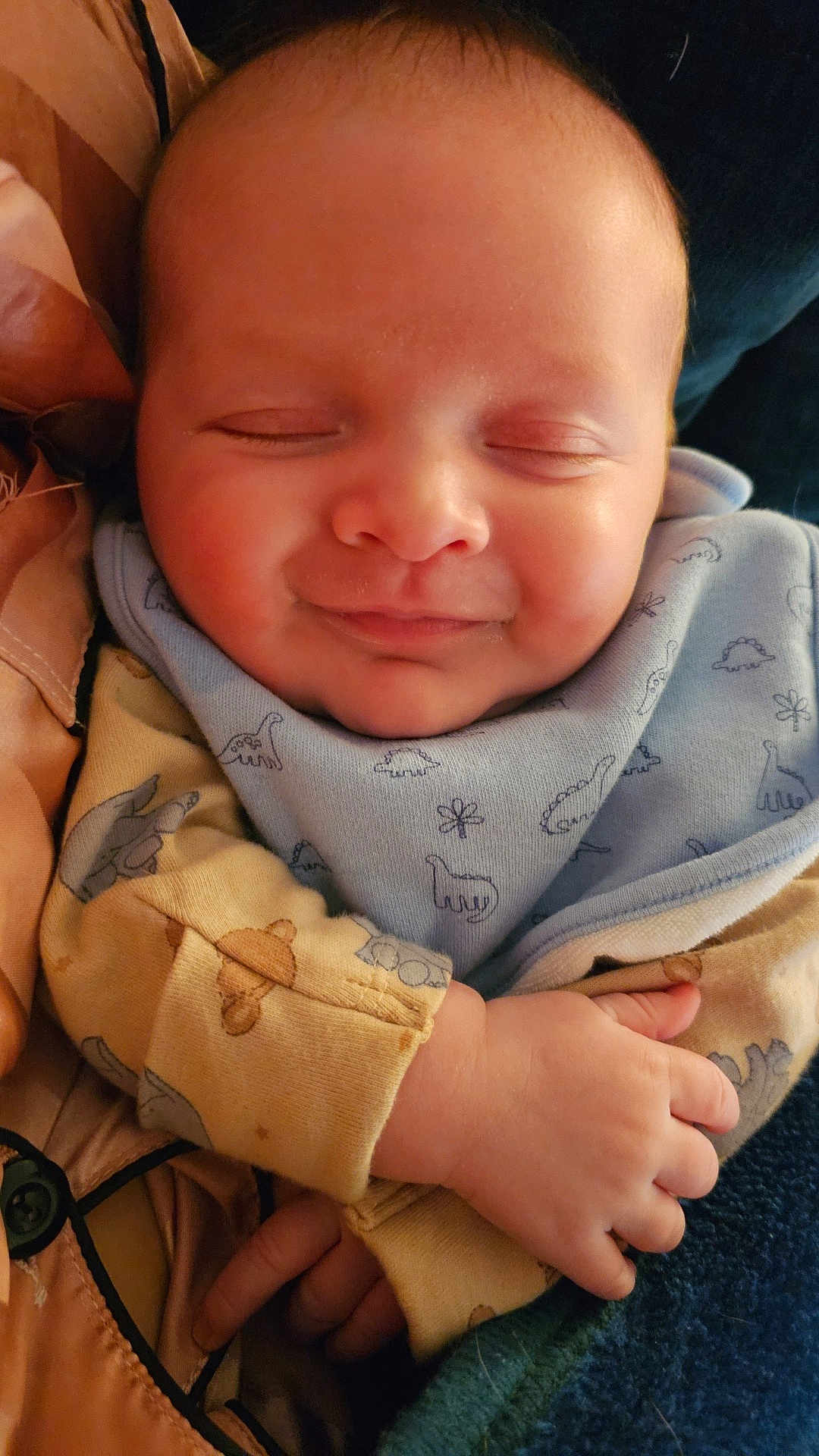 Arthur is registered to the contest to win money with this photo: baby, infant, sleeping, smile, face, hand, clothing, bib, dinosaur_print, cute, cozy, child, portrait, warm, soft_lighting, closeup, skin, newborn, peaceful, resting