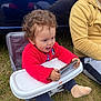 bright_starts, casual_clothing, child, curly_hair, daylight, feet, grass, happy, high_chair, outdoor, person, playful, red_sweater, reflection, sitting, smartphone, sock, toddler, toy, yellow_hoodie