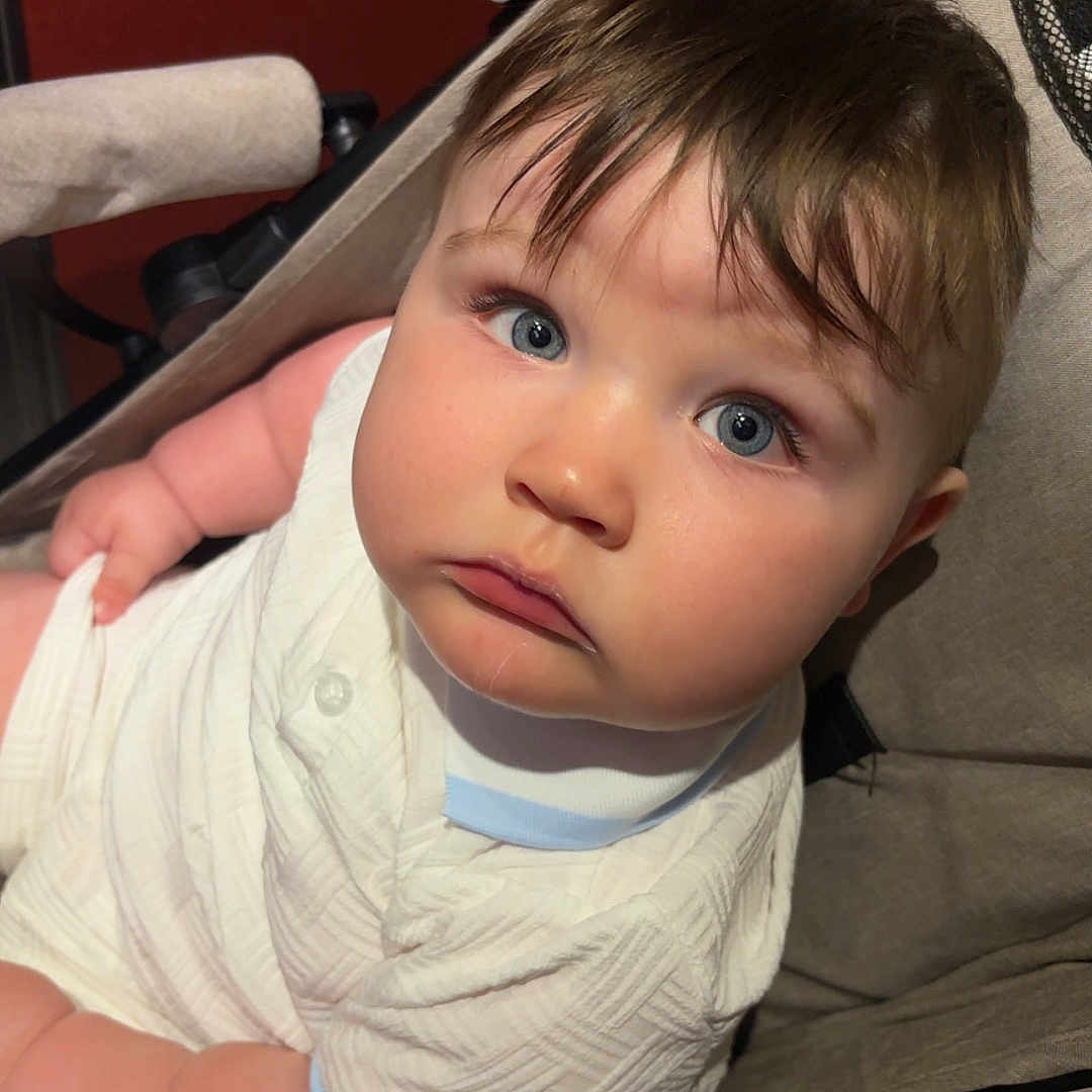 Robbie joined the competition — help win amazing prizes! baby, blue_eyes, child, chubby_cheeks, close_up, curly_hair, cute, expression, face, hands, indoor, infant, person, portrait, seat, skin, soft_lighting, stroller, white_clothing, young_child