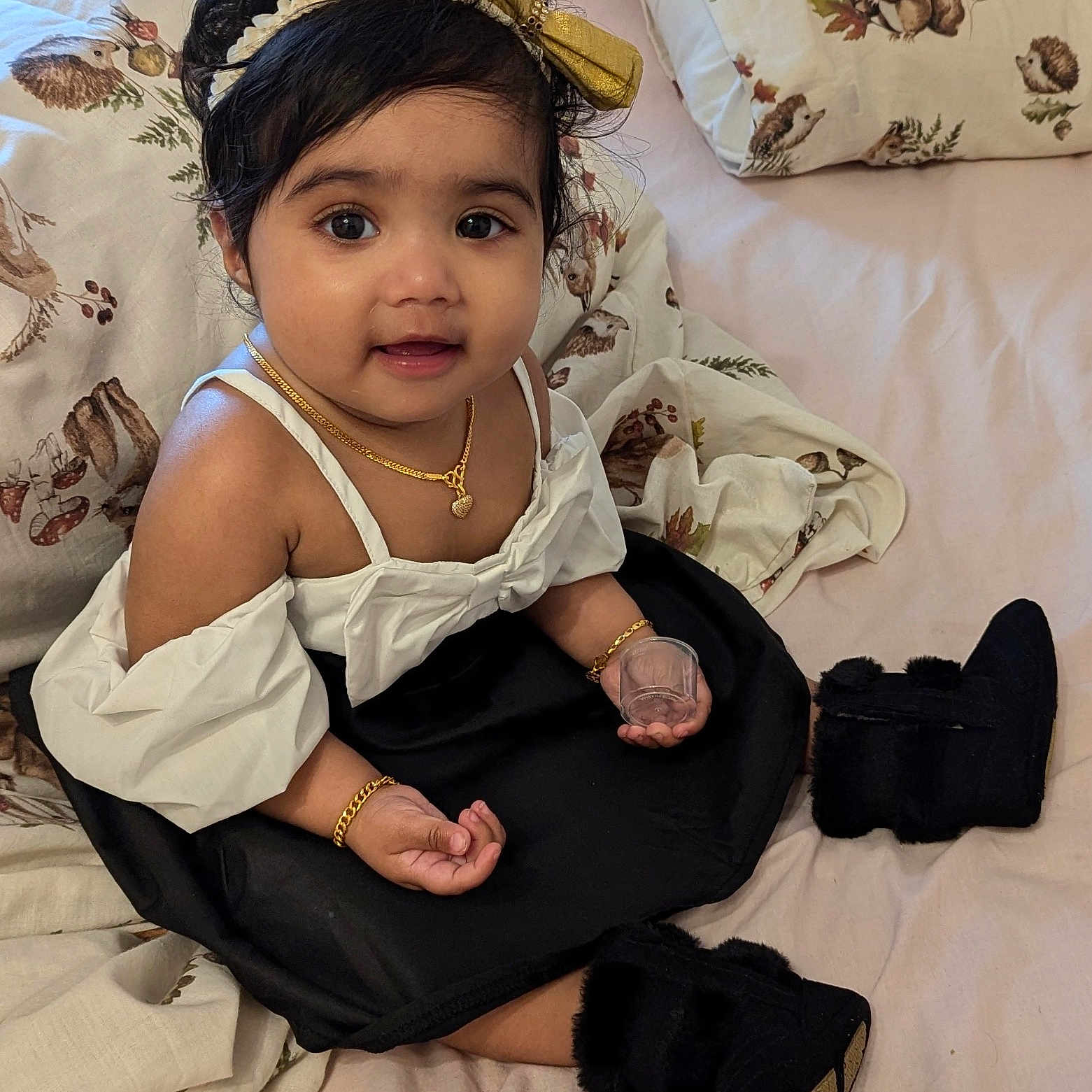 Hanika is registered to the contest to win money with this photo: animal_print, baby, bed, black_hair, blanket, boots, child, curious, cute, dress, girl, gold_jewelry, hand, headband, indoor, person, pillow, portrait, sitting, smiling