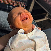 Marnie is registered to the contest to win money with this photo: baby, infant, smiling, laughing, onesie, heart_pattern, hand, laptop, cartoon, indoor, child, cute, joyful, happy, person, face, clothing, technology, blurred_background, cozy