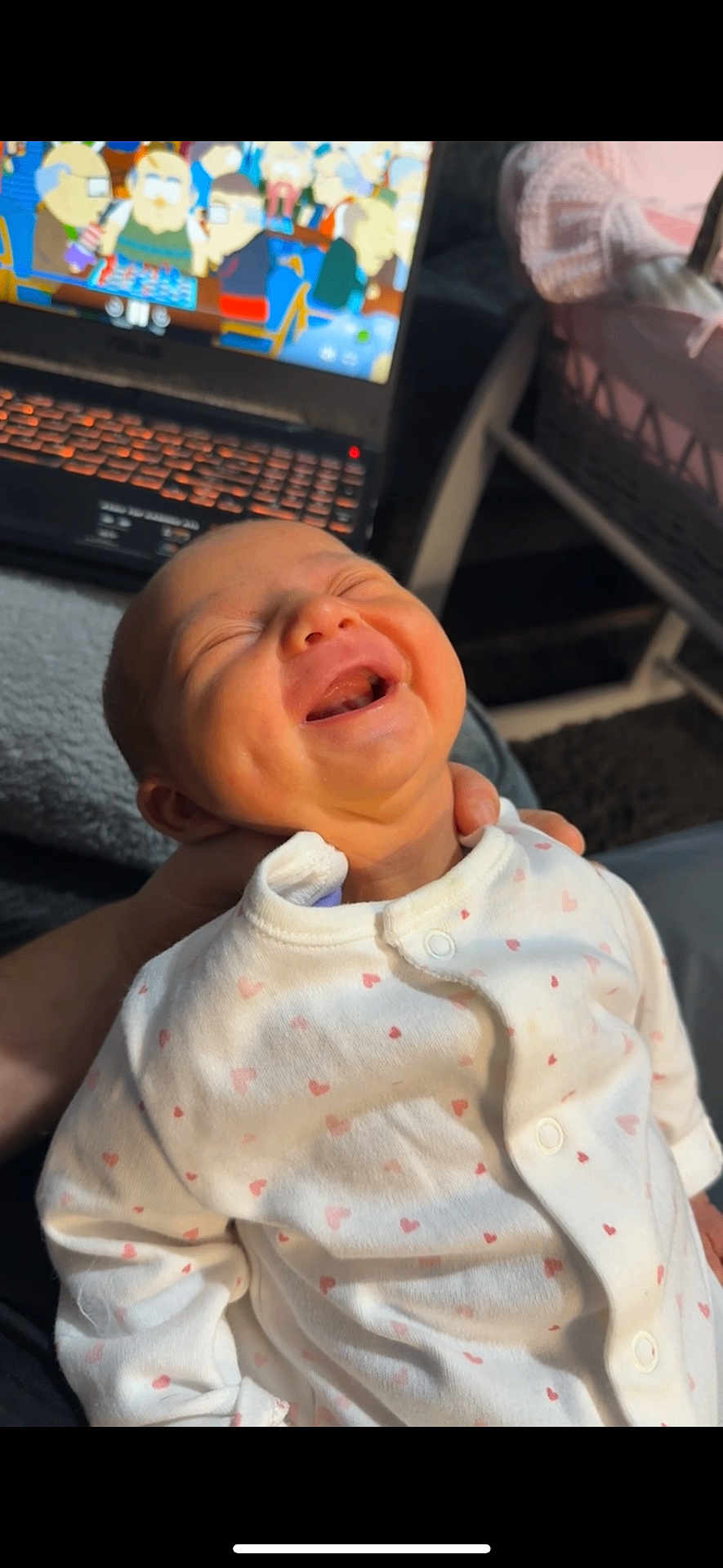 Marnie is registered to the contest to win money with this photo: baby, infant, smiling, laughing, onesie, heart_pattern, hand, laptop, cartoon, indoor, child, cute, joyful, happy, person, face, clothing, technology, blurred_background, cozy