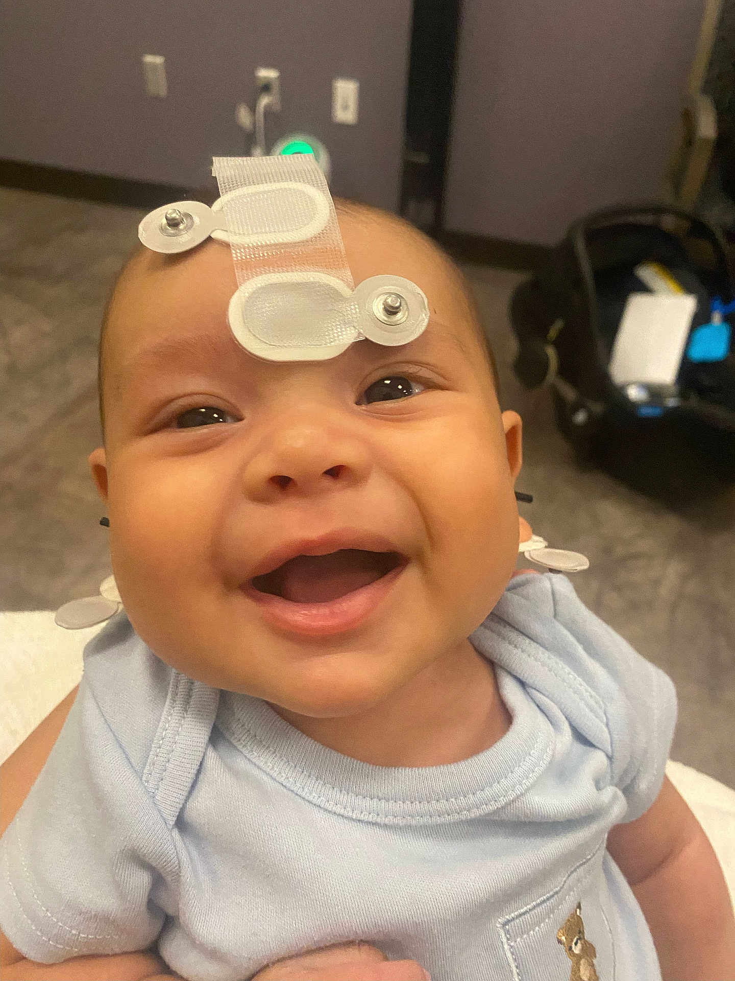 Jasiel joined the competition — help win amazing prizes! baby, smiling, face, indoor, medical_sensor, clothing, blue_shirt, person, child, happy, infant, cute, closeup, head, eyes, mouth, skin, baby_girl, baby_boy, newborn