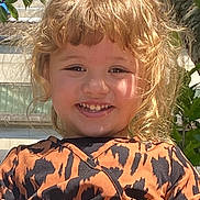 Assil a rejoint le concours — aidez-le/la à gagner de superbes lots ! child, smiling, blonde_hair, curly_hair, dress, orange_dress, patterned_clothing, outdoor, tree, leaves, sunny, happy, portrait, person, nature, daylight, face, cute, young_child, fashion