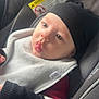 baby, child, car_seat, beanie, bib, clothing, seatbelt, infant, face, expression, light, soft_light, indoors, cute, portrait, person, warm_clothing, bundle, seat, young