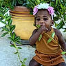 toddler, child, flower_headband, leaf, plant, pot, outdoor, curious, sitting, brown_clothing, nature, greenery, cute, exploring, face, portrait, young_child, headwear, plant_pot, daylight