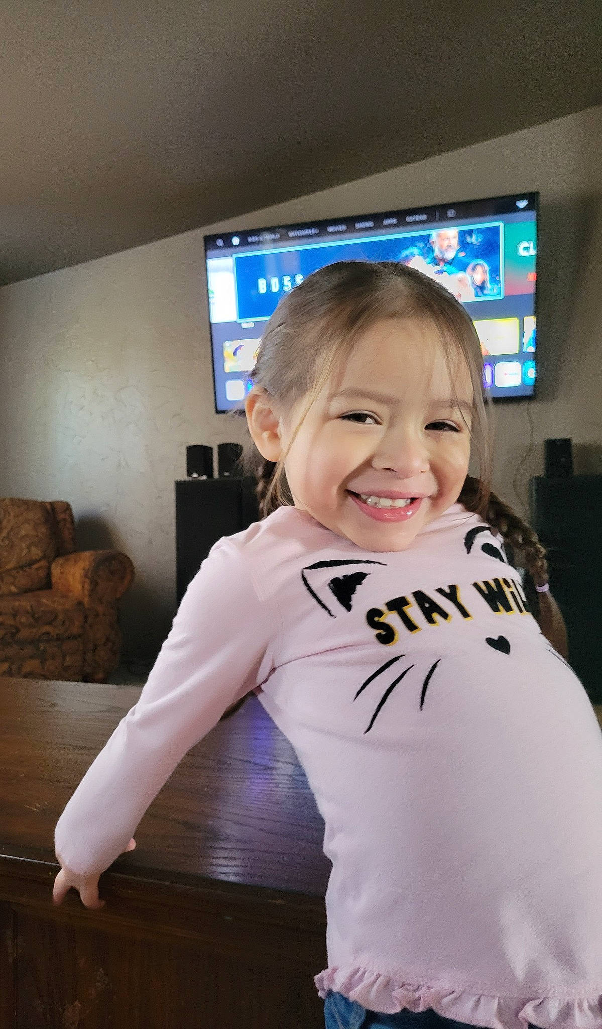 Juniper is registered to the contest to win money with this photo: abdomen, child, couch, display_device, electric_blue, flooring, fun, gadget, happy, hardwood, jersey, joy, person, room, sleeve, smile, sportswear, t_shirt, television, television_set