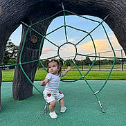 Deniz joined the competition — help win amazing prizes! child, toddler, playground, rope_structure, green_rope, outdoor, grass, sky, clouds, sunset, pigtails, white_shirt, shorts, shoes, fence, playing, young_child, park, fun, daylight